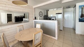 Una cocina moderna con una isla central, un comedor con una mesa redonda y sillas, y un espejo grande sobre la isla.