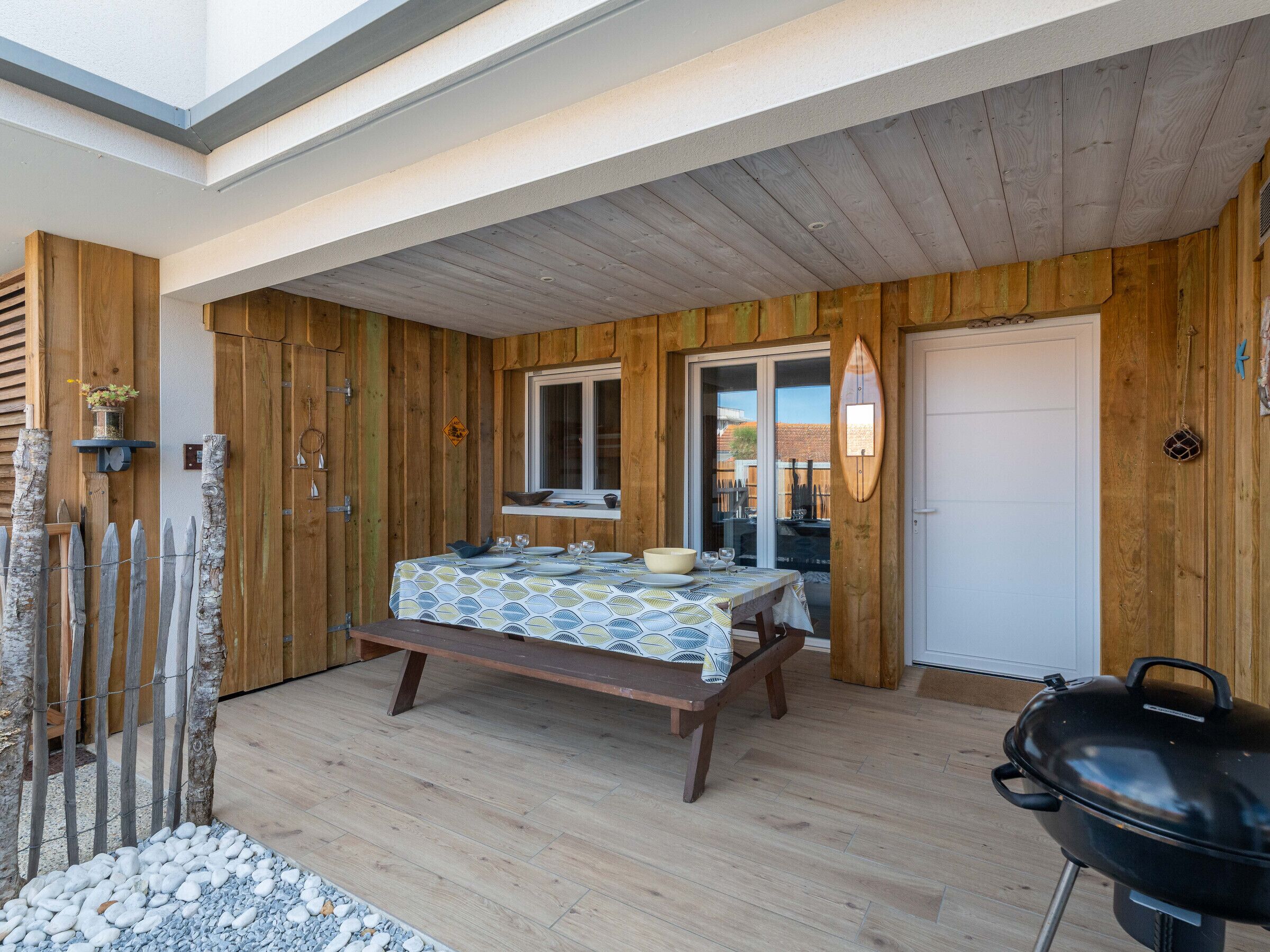 A wooden interior with a dining table set for four, a barbecue grill, and a window overlooking a garden.
