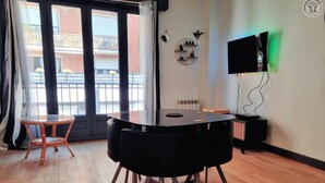 A room with a round table, a television mounted on the wall, and a view of a balcony with a railing. - Zen Duplex in Valenciennes city center (Valenciennes)