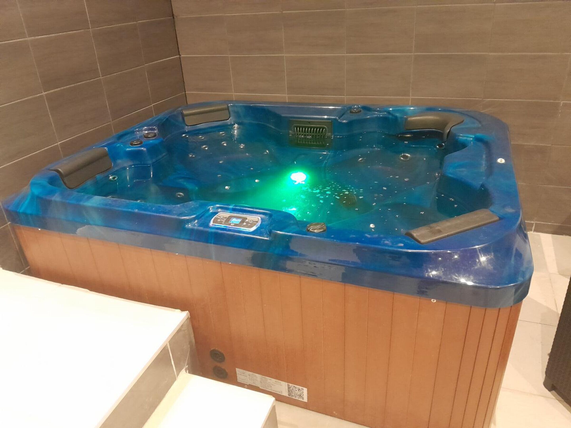 Un bain à remous doté d’un panneau de commande numérique, entouré de murs recouverts de carreaux.