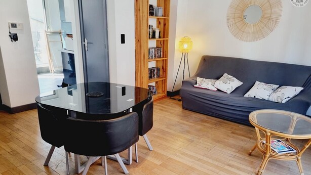 A modern living room with a glass-top dining table, a dark grey sofa, and a wicker side table. - Zen Duplex in Valenciennes city center (Valenciennes)