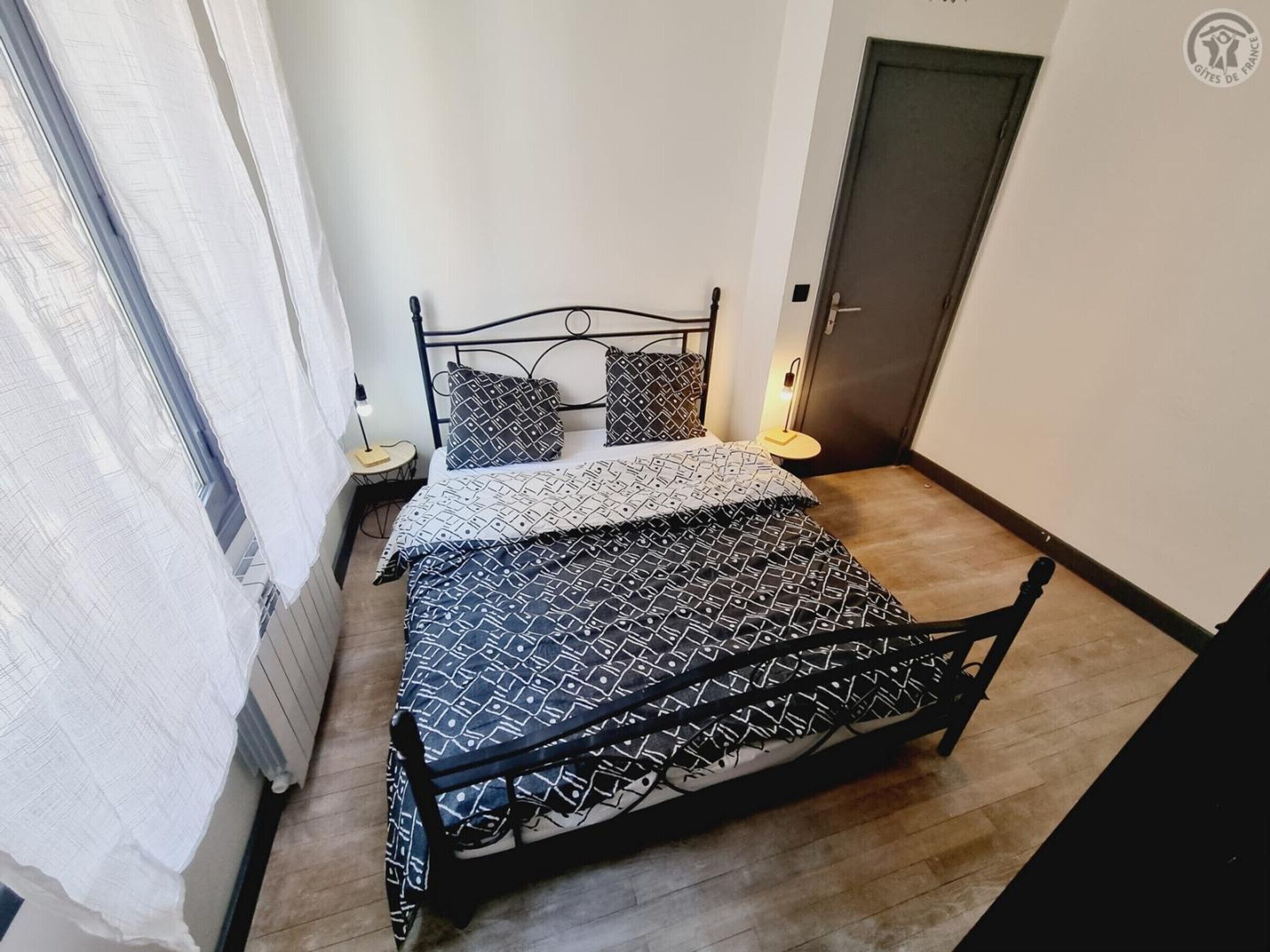 Un dormitorio con cama, dos mesitas de noche, una puerta y una ventana con cortinas.
