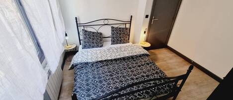 Un dormitorio con cama, dos mesitas de noche, una puerta y una ventana con cortinas.
