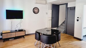A modern living room with a flat-screen TV, a round table with chairs, a wall clock, and a staircase leading to another level. - Zen Duplex in Valenciennes city center (Valenciennes)