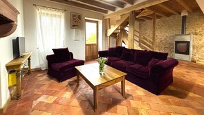 A cozy living room with a wooden ceiling, a stone fireplace, and a staircase.