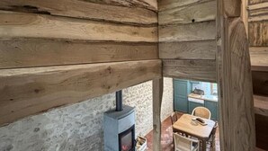 A rustic cabin interior with wooden walls, a stone wall, a fireplace, and a dining area with a table and chairs.