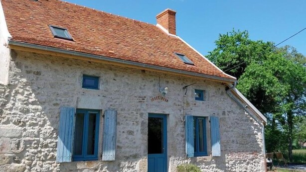 A stone building with a tiled roof, a central door, and two windows with shutters.