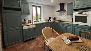 A kitchen with teal cabinets, a wooden dining table with a loaf of bread, and a window with a view of greenery.