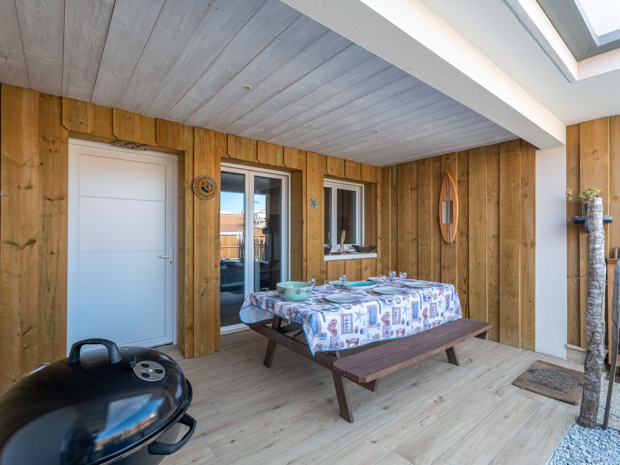 Una habitación con paneles de madera y una puerta corrediza de vidrio que da a un balcón, una parrilla y una mesa con mantel estampado.
