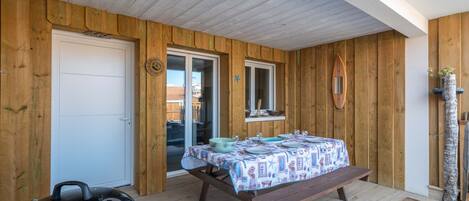 Una habitación con paneles de madera y una puerta corrediza de vidrio que da a un balcón, una parrilla y una mesa con mantel estampado.