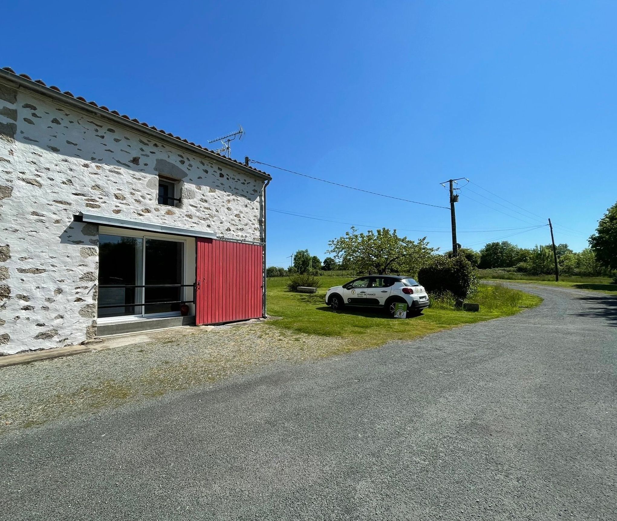 A rural road with a white building featuring a red door and a parked car.
