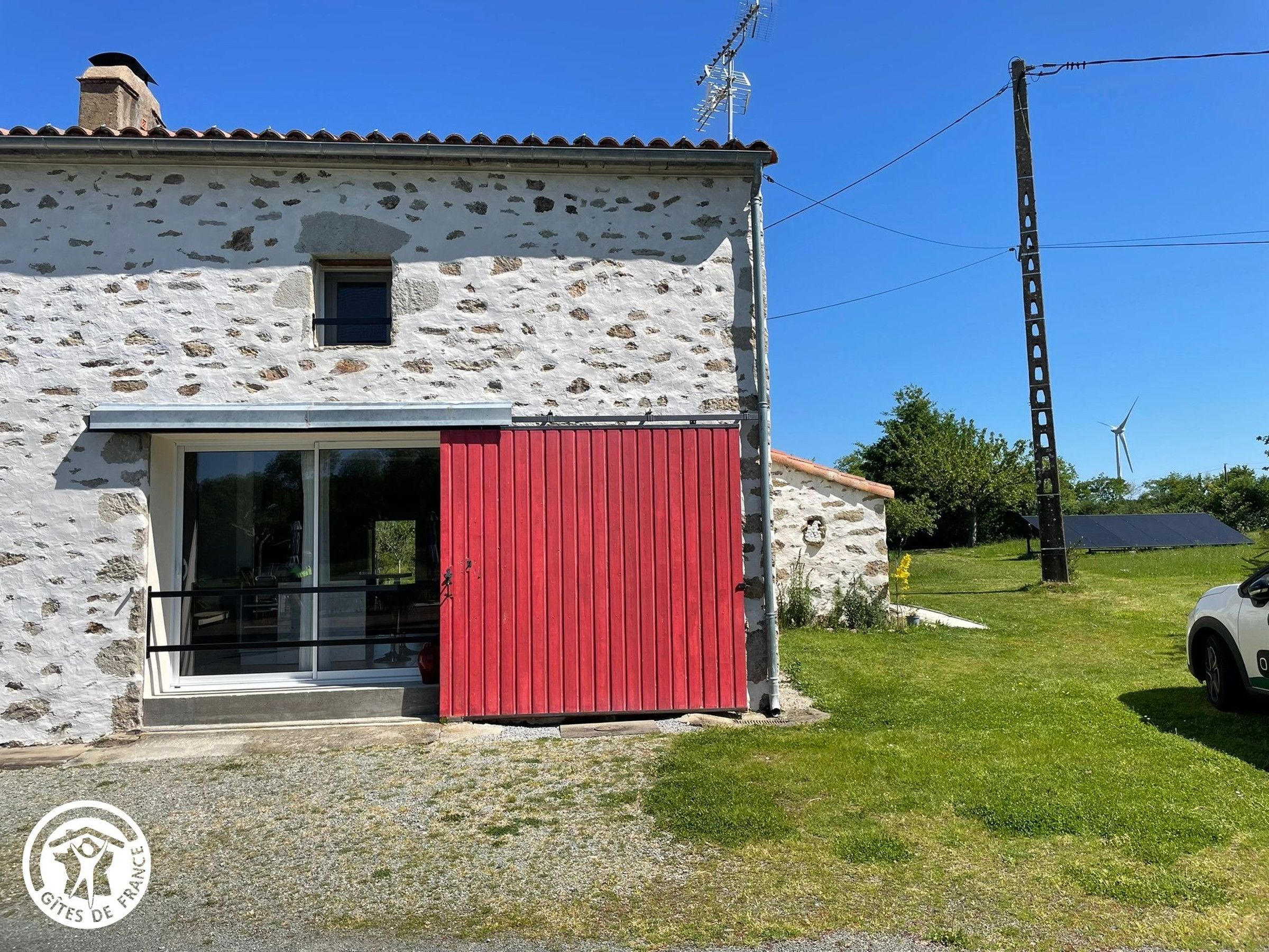Un edificio rustico in pietra con una porta rossa, una piccola finestra e un'antenna metallica.