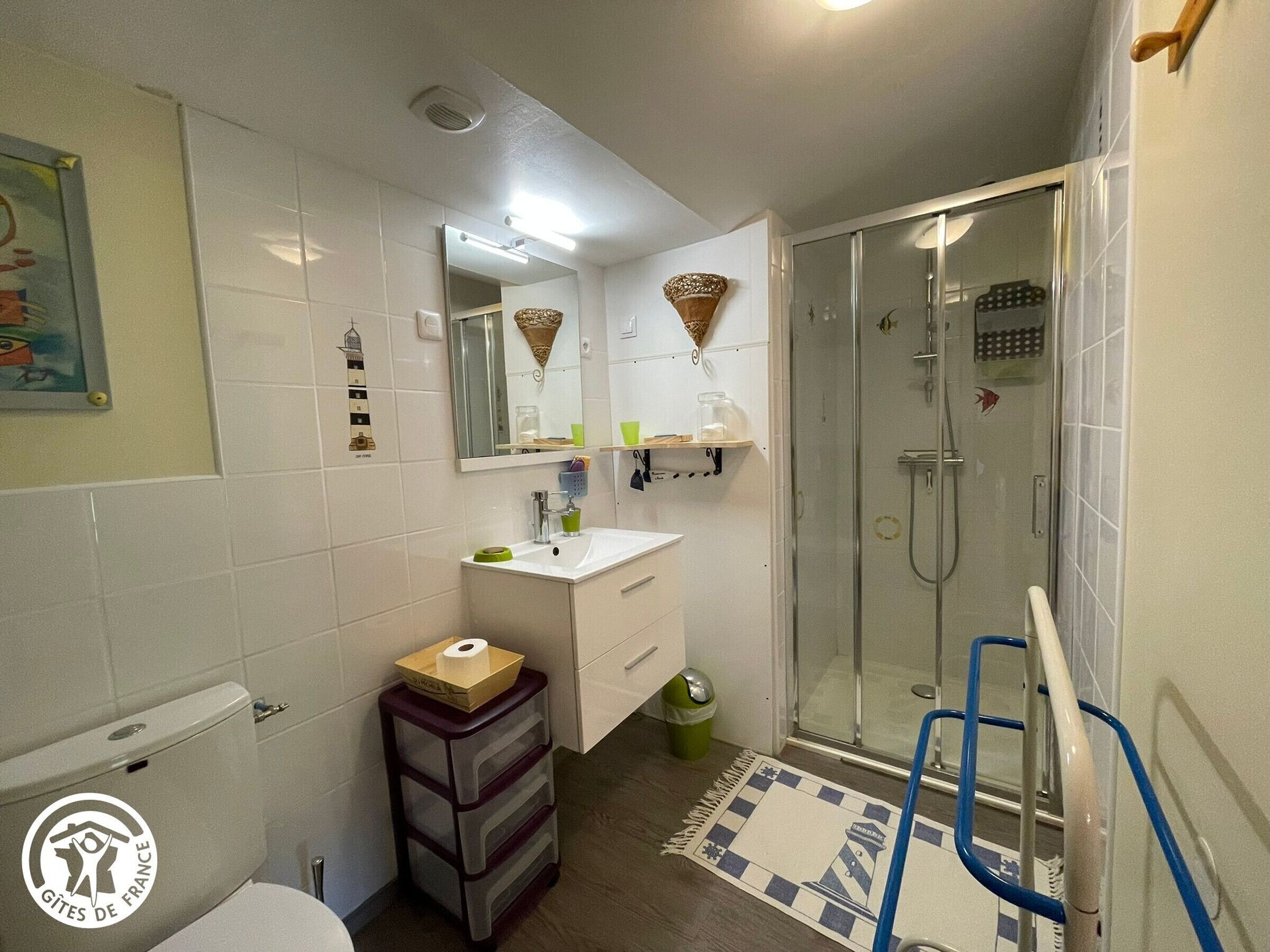 Ein Badezimmer mit Toilette, Waschbecken, Spiegel, Dusche und einem kleinen Mülleimer.
