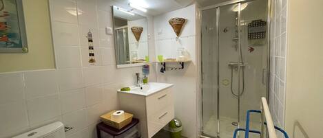 Ein Badezimmer mit Toilette, Waschbecken, Spiegel, Dusche und einem kleinen Mülleimer.