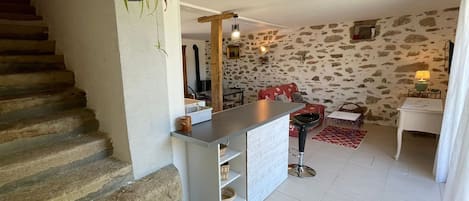 Una escalera de piedra conduce a una sala de estar con una isla de cocina, un sofá rojo y una pared de piedra.