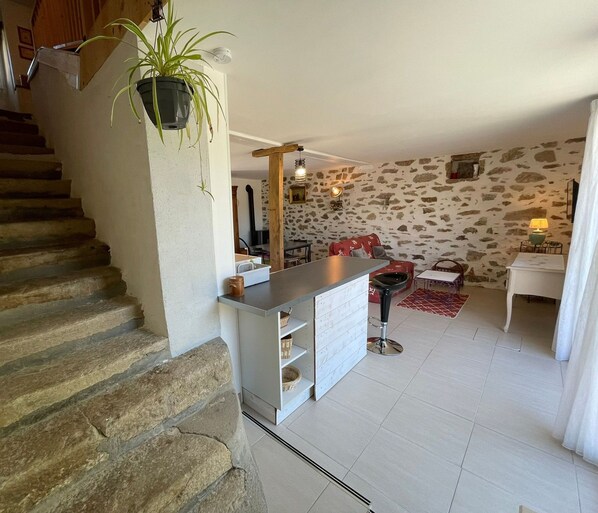 A stone staircase leading to a living area with a kitchen island, a red sofa, and a stone wall. - Charming Cottage in Beaufou with Private Terrace (Beaufou)