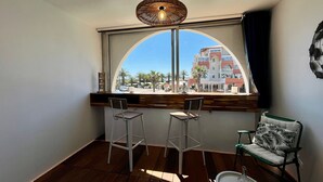 A corner room with a large window, two bar stools, a chair, and a small table.