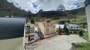 Un paysage montagneux avec des sommets enneigés en arrière-plan, une aire de stationnement et des bâtiments aux toits plats.