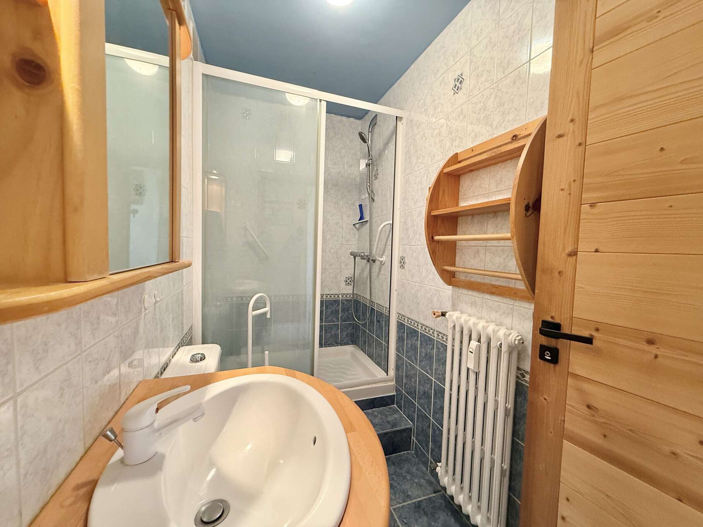 A bathroom with a white sink, a glass shower enclosure, and a wooden door.
