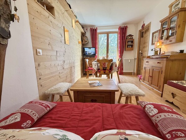 Una habitación acogedora con pared de madera, una mesa de comedor de madera con sillas, un televisor y un armario con cajones.