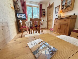 A cozy room with wooden walls, a dining table with a magazine, a TV, and a wooden cabinet.