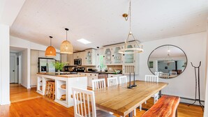 Une cuisine moderne avec des meubles blancs, une table à manger en bois et des luminaires suspendus.