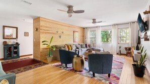Un salon moderne avec un plancher en bois, un ensemble de canapés, deux fauteuils, une table basse et un téléviseur fixé au mur.