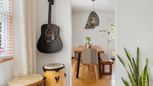Une pièce avec une guitare, une batterie, une table à manger avec des chaises et un luminaire suspendu.
