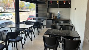 A modern cafe with black marble tables and chairs, a water dispenser, and a view of the street outside. - Cim Pansiyon (Antalya)