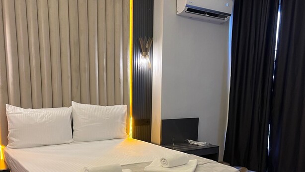 A neatly made bed with white linens and towels, a modern air conditioning unit, and a wooden floor. - Cim Pansiyon (Antalya)