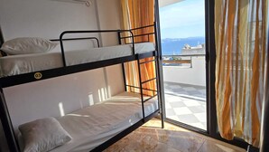 A dormitory room with bunk beds, a window with curtains, and a view of the sea.
