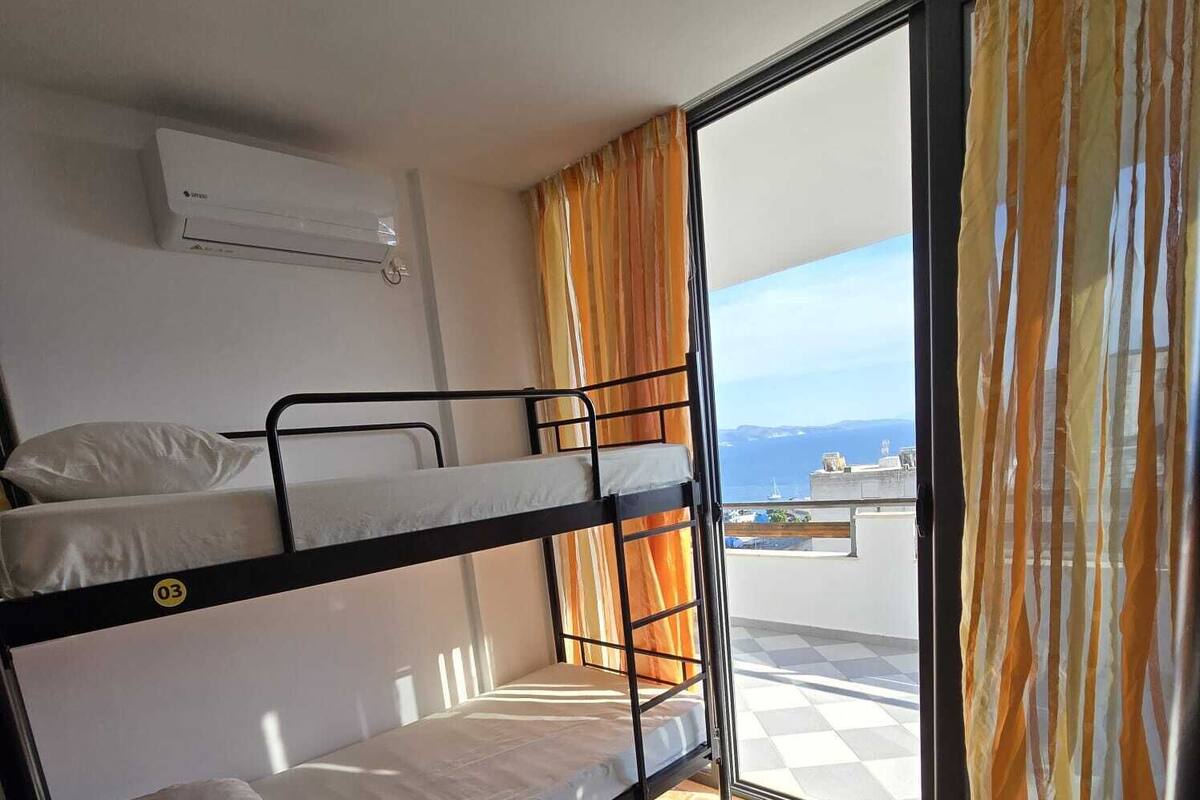 A dormitory room with bunk beds, a window with curtains, and a view of the sea.