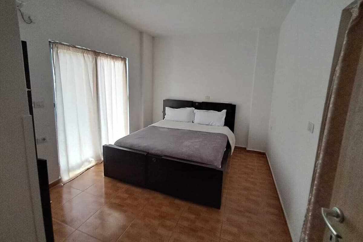 A bedroom with a bed, a window with curtains, and a door.