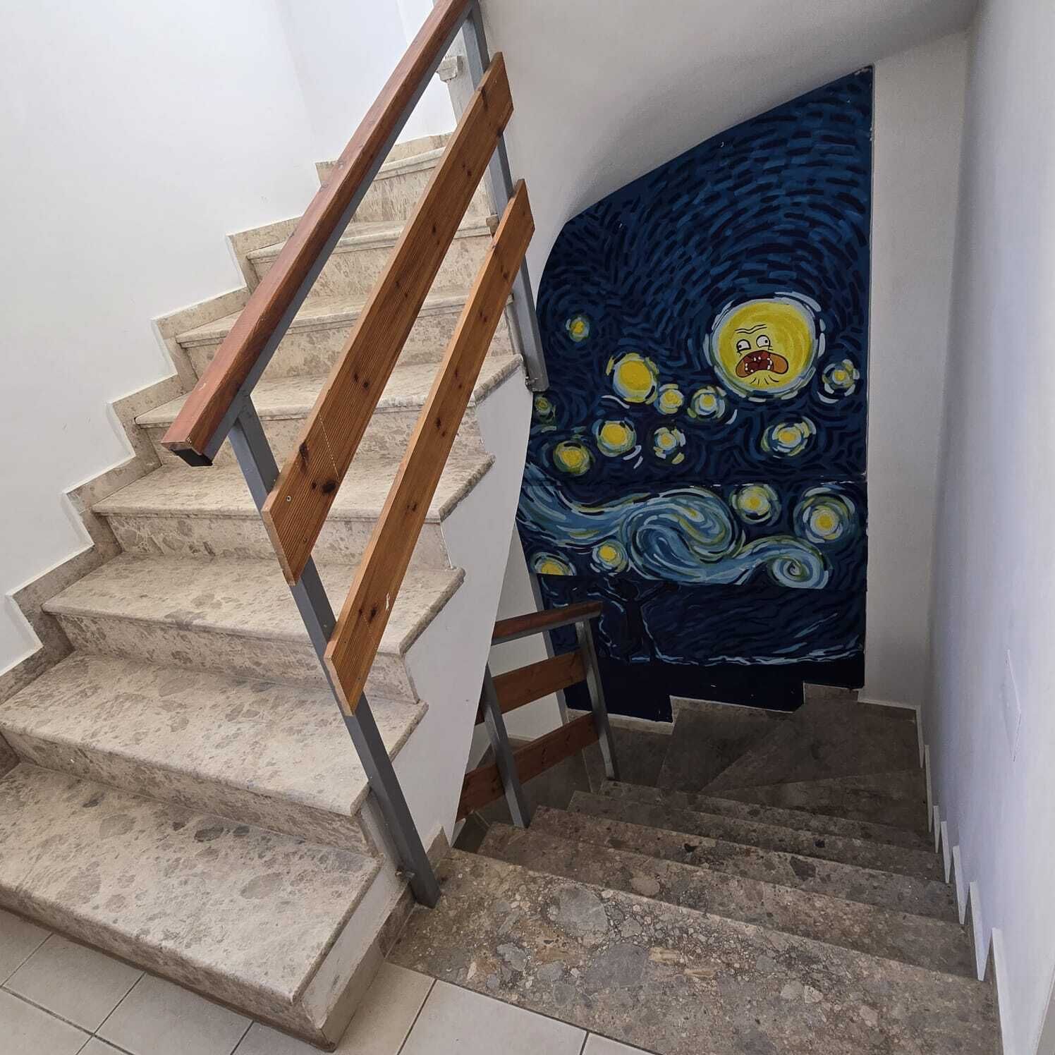 Una escalera con barandilla de madera y pared azul con un cuadro.