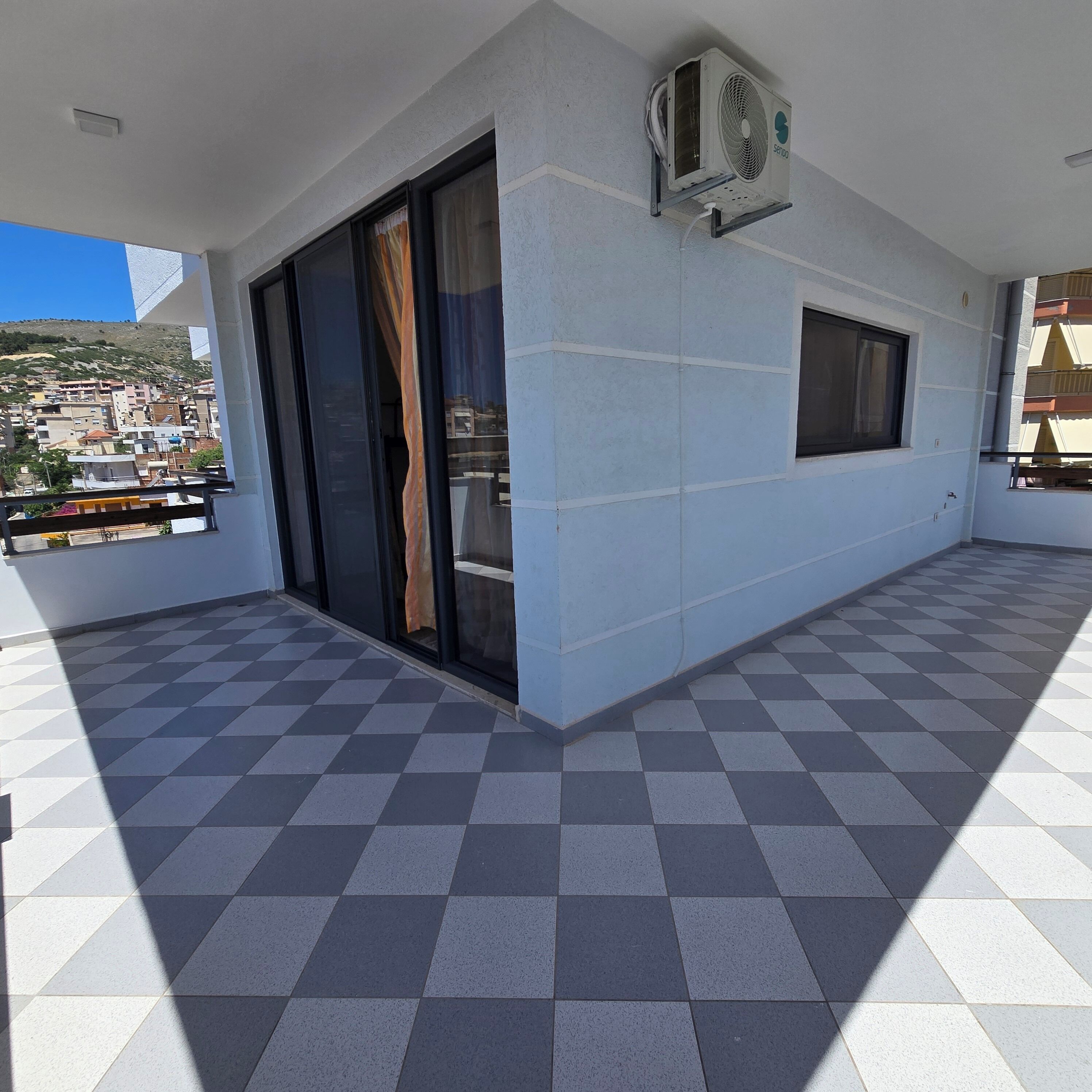 Un balcón con piso a cuadros, una puerta corredera de vidrio y un equipo de aire acondicionado en la pared.
