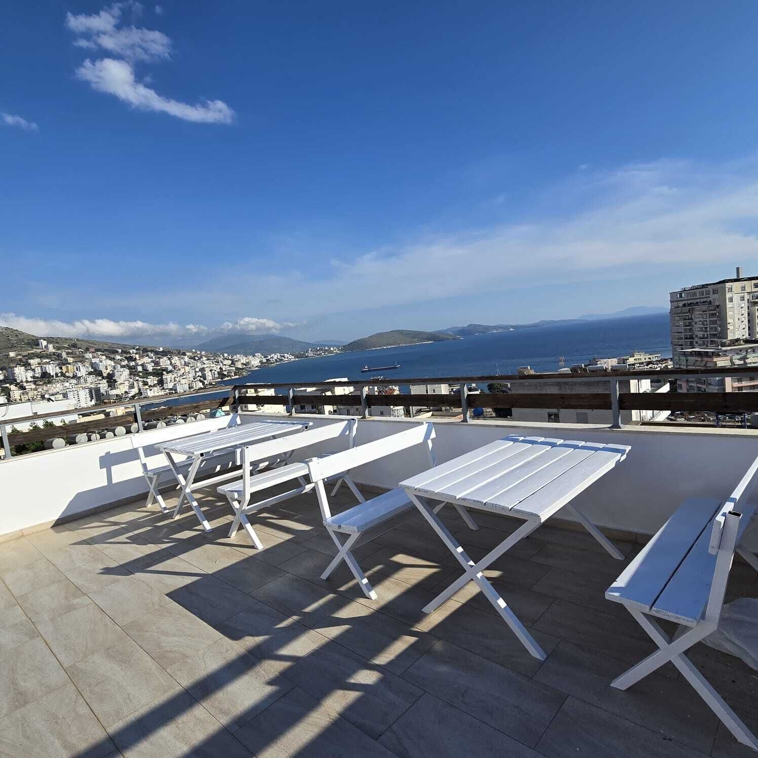 Une terrasse sur le toit, dotée de chaises longues blanches et offrant une vue sur une ville côtière et la mer.