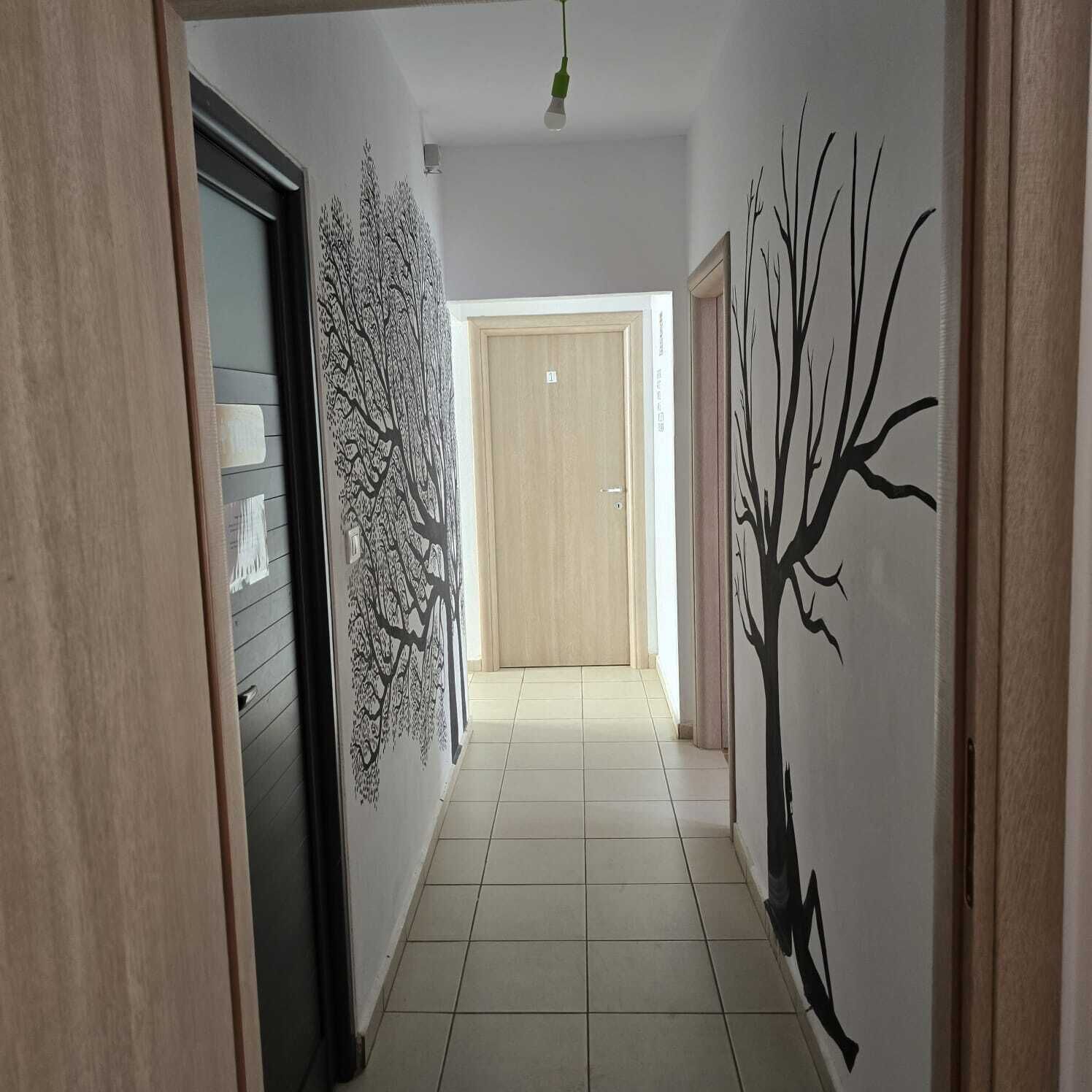 A hallway with a tiled floor, a door with a number, and a wall with a tree decal.