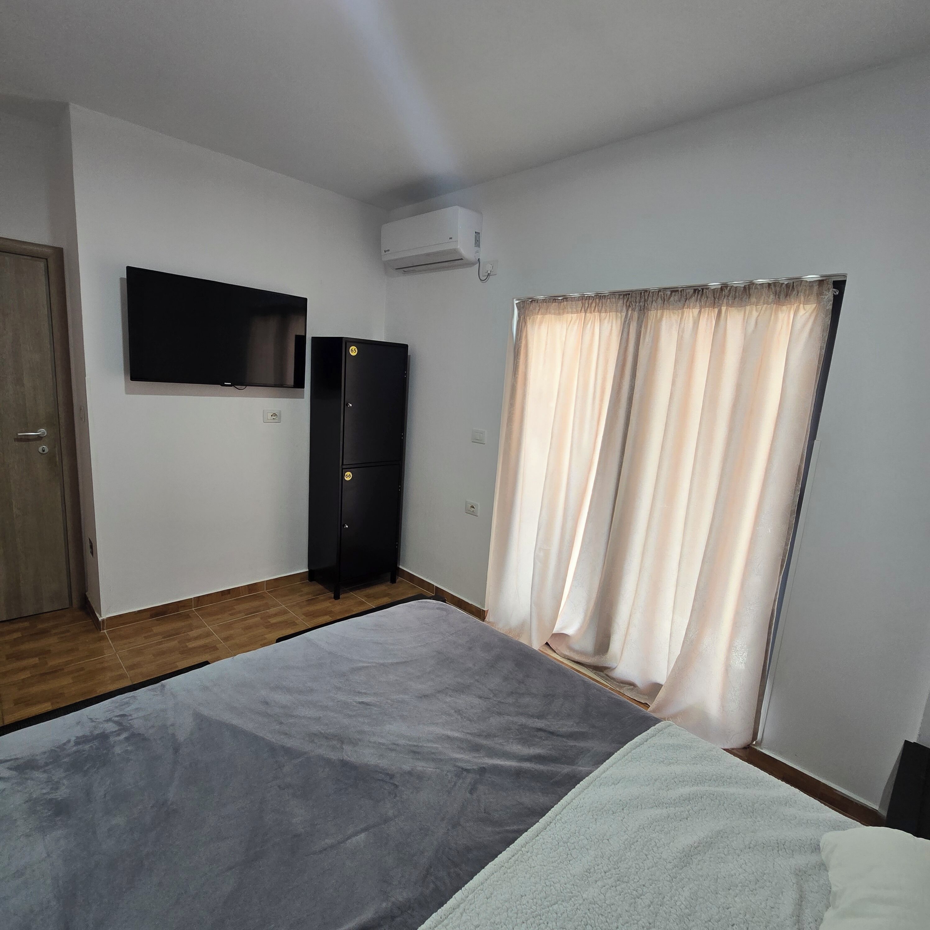 A bedroom with a bed, a television, a wardrobe, and a window with curtains.