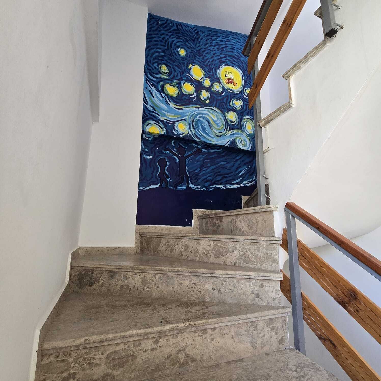 Un escalier orné d’un tableau bleu représentant une scène nocturne avec des étoiles et un arbre.