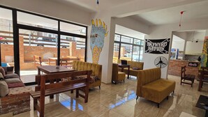 A spacious indoor area with a wooden dining table, yellow sofas, and a large window providing a view of the outside.