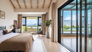 A modern hotel room with a large bed, a view of the cityscape, and a balcony with a mountain view.