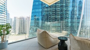 A modern living room with a large glass window, a potted plant, and a beige sofa. - Upscale 1BR Luxury Apt in Missoni Urban Oasis (Dubai)