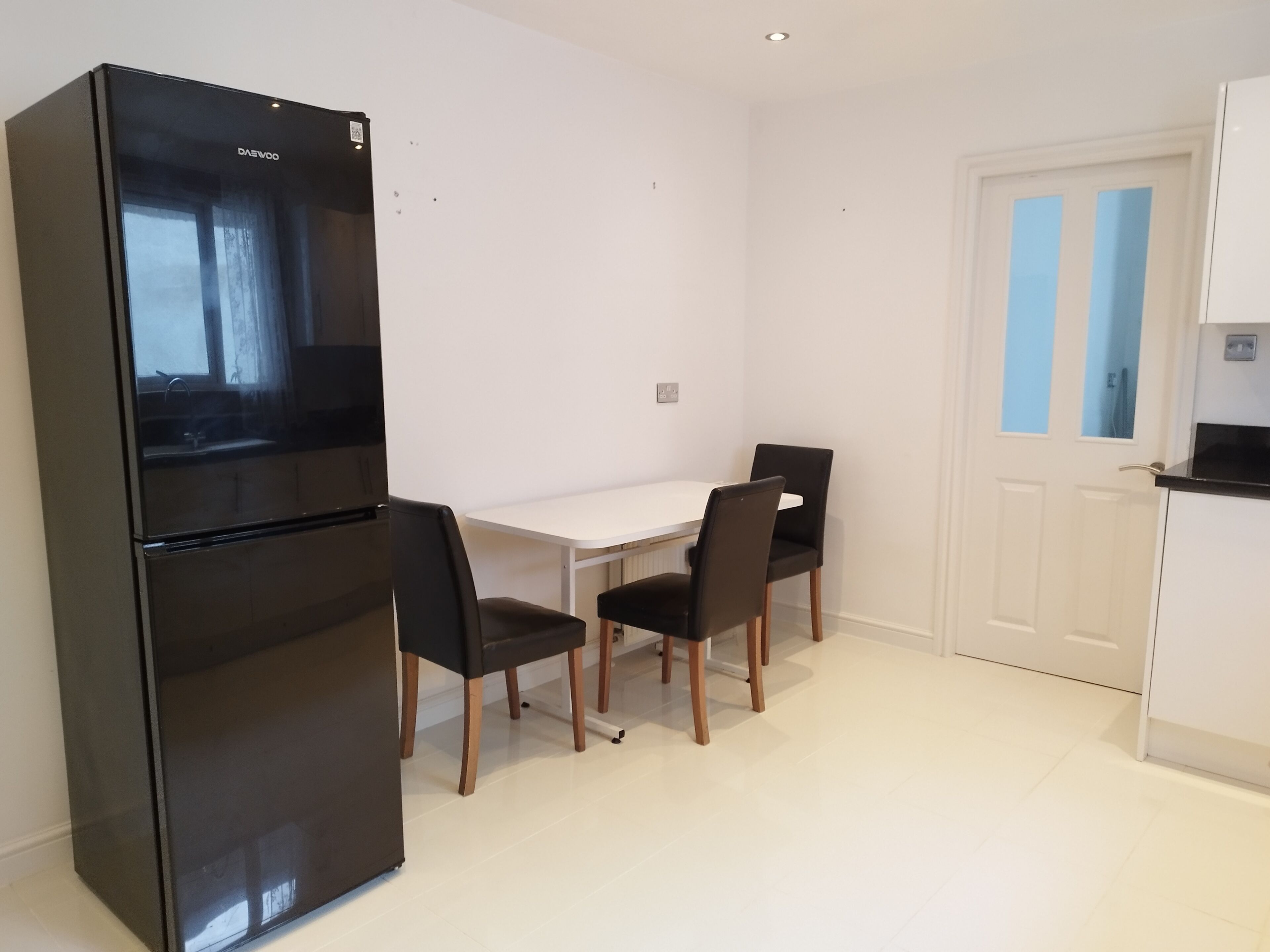 A compact kitchen with a black refrigerator, a white dining table, and two black chairs.