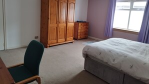 Une chambre à coucher comprenant un lit, une armoire en bois, une commode, une chaise et une fenêtre avec des rideaux.