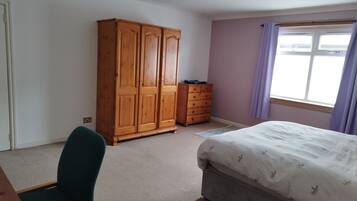 Ein Schlafzimmer mit einem Bett, einem Holzschrank, einem Schminktisch, einem Stuhl und einem Fenster mit Vorhängen.