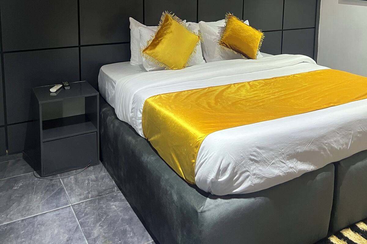 Een moderne slaapkamer met een groot bed, nachtkastje en een donker hoofdeinde.