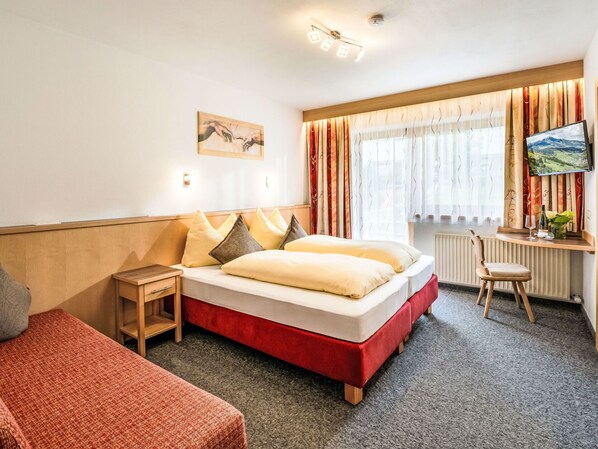 A hotel room with a bed, a desk, a chair, a TV, and a window with curtains.