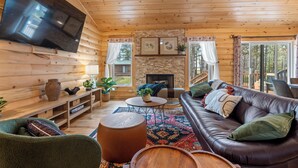 Ein gemütliches Cabin-Interieur mit einem großen Fernseher, Holzwänden, einem Kamin, einem Ledersofa und einem Essbereich.