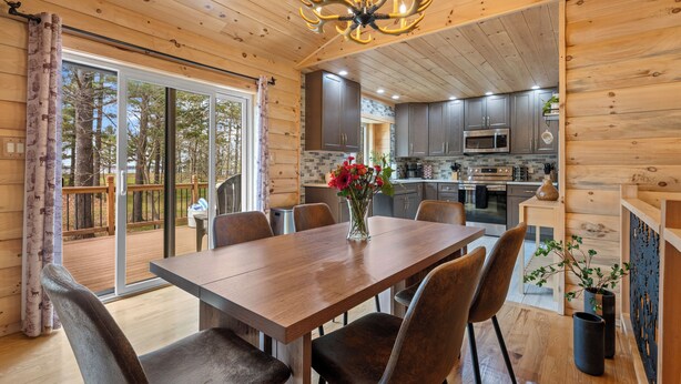Ein Holzblockhaus-Interieur mit Esstisch, Stühlen, einer Chandelierleuchtre und einer Küchenzeile.
