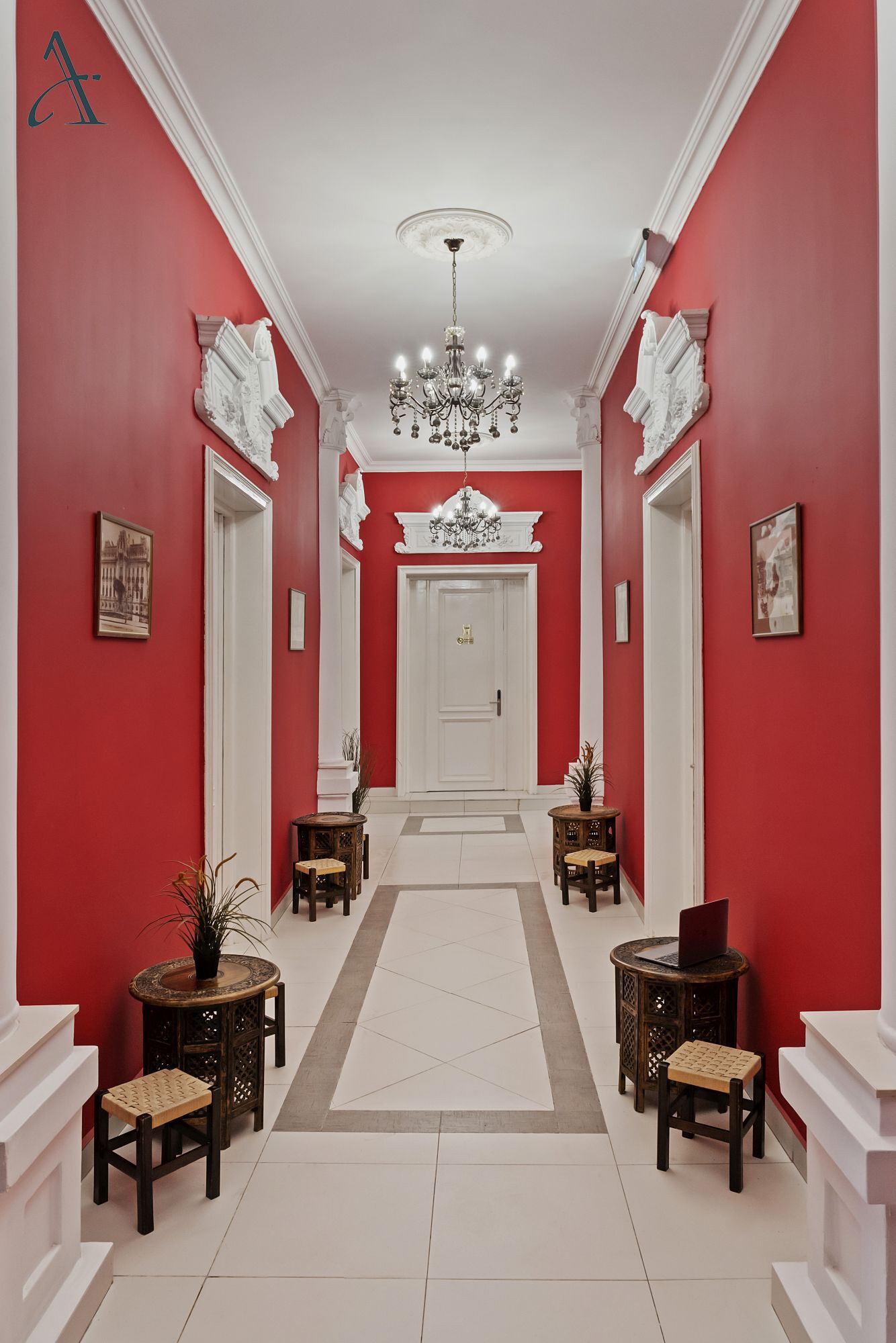 A hallway with red walls, white trim, a chandelier, and a white door at the end.
